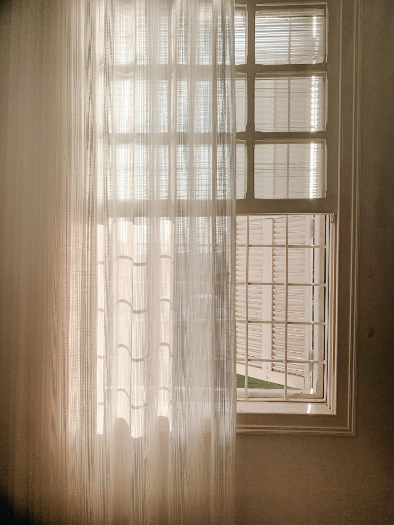 Image shows open sash window, with a curtain pulled halfway shut. 